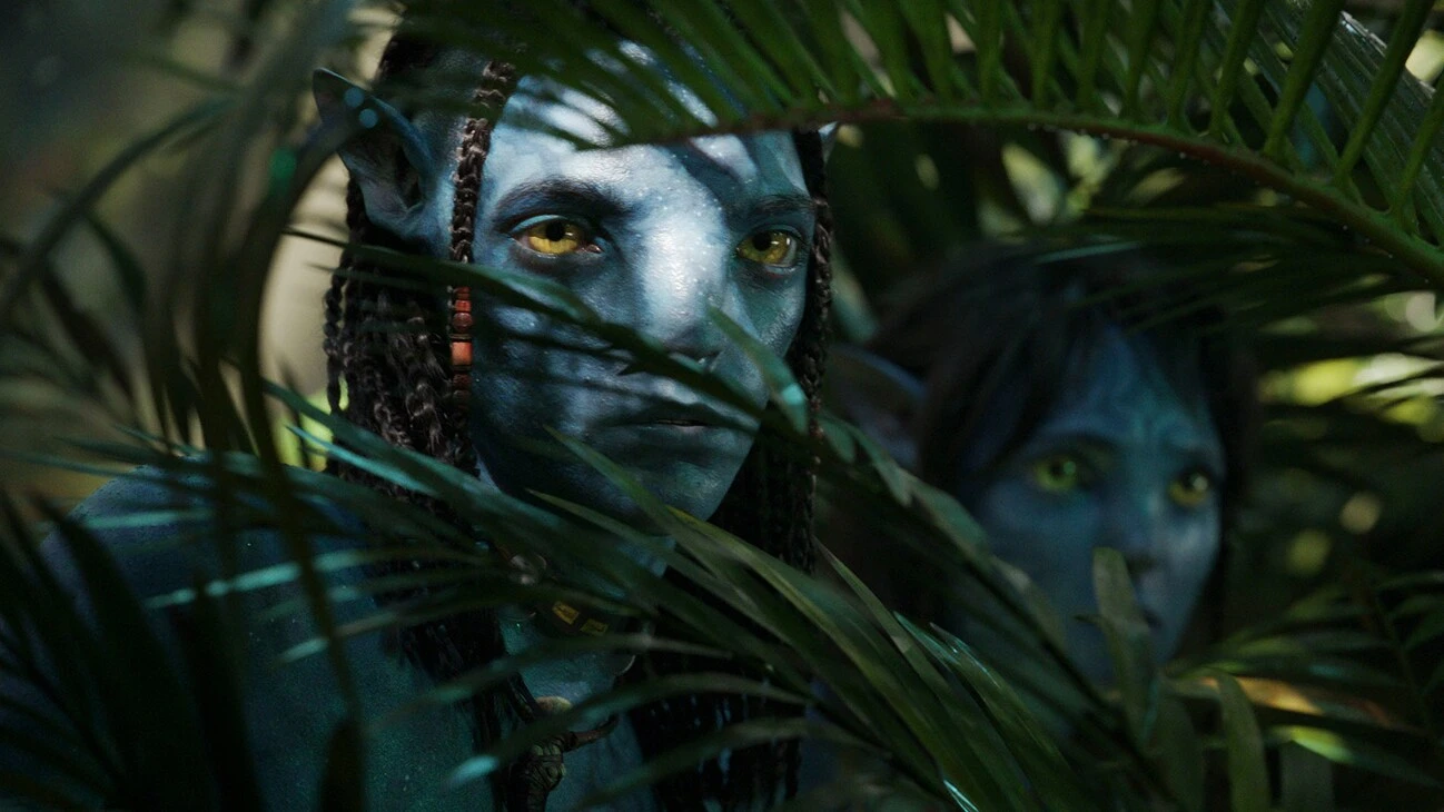 Image of two characters peering through branches from the 20th Century Studios movie Avatar: The Way of Water.